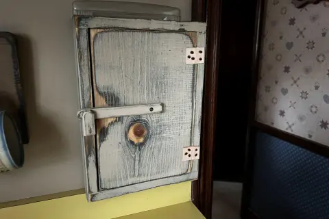 Drewniana szafka na licznik elektryczny, stylizowana na rustykalną, z widocznym zamkiem i zawiasami.